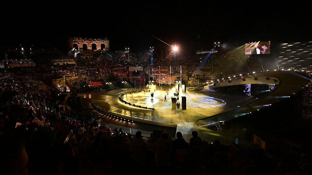 Spettacolo serale durante la cerimonia di chiusura delle Olimpiadi Invernali Milano-Cortina 2026 con palco illuminato e pubblico sugli spalti