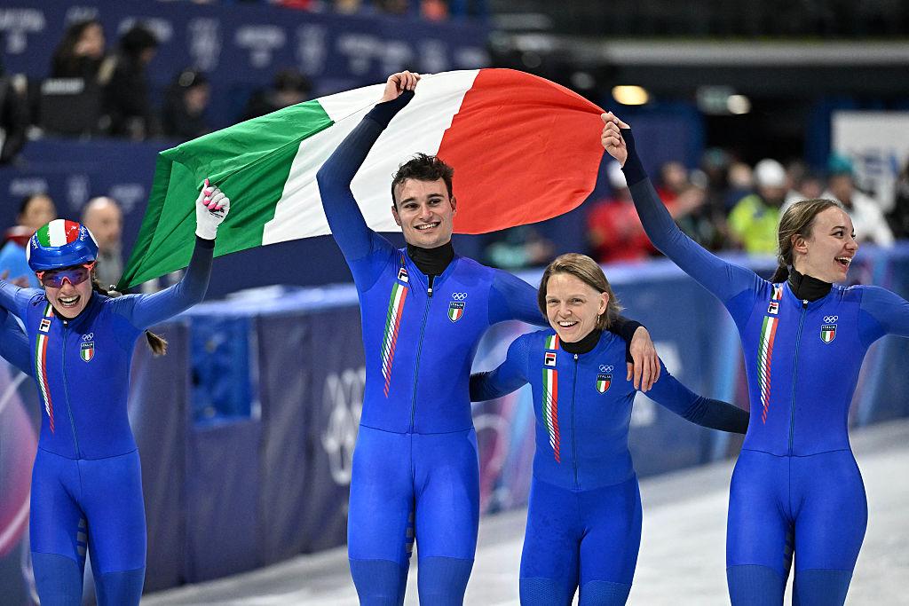 Atleti italiani esultano con la bandiera tricolore dopo la medaglia nello short track alle Olimpiadi Milano Cortina 2026